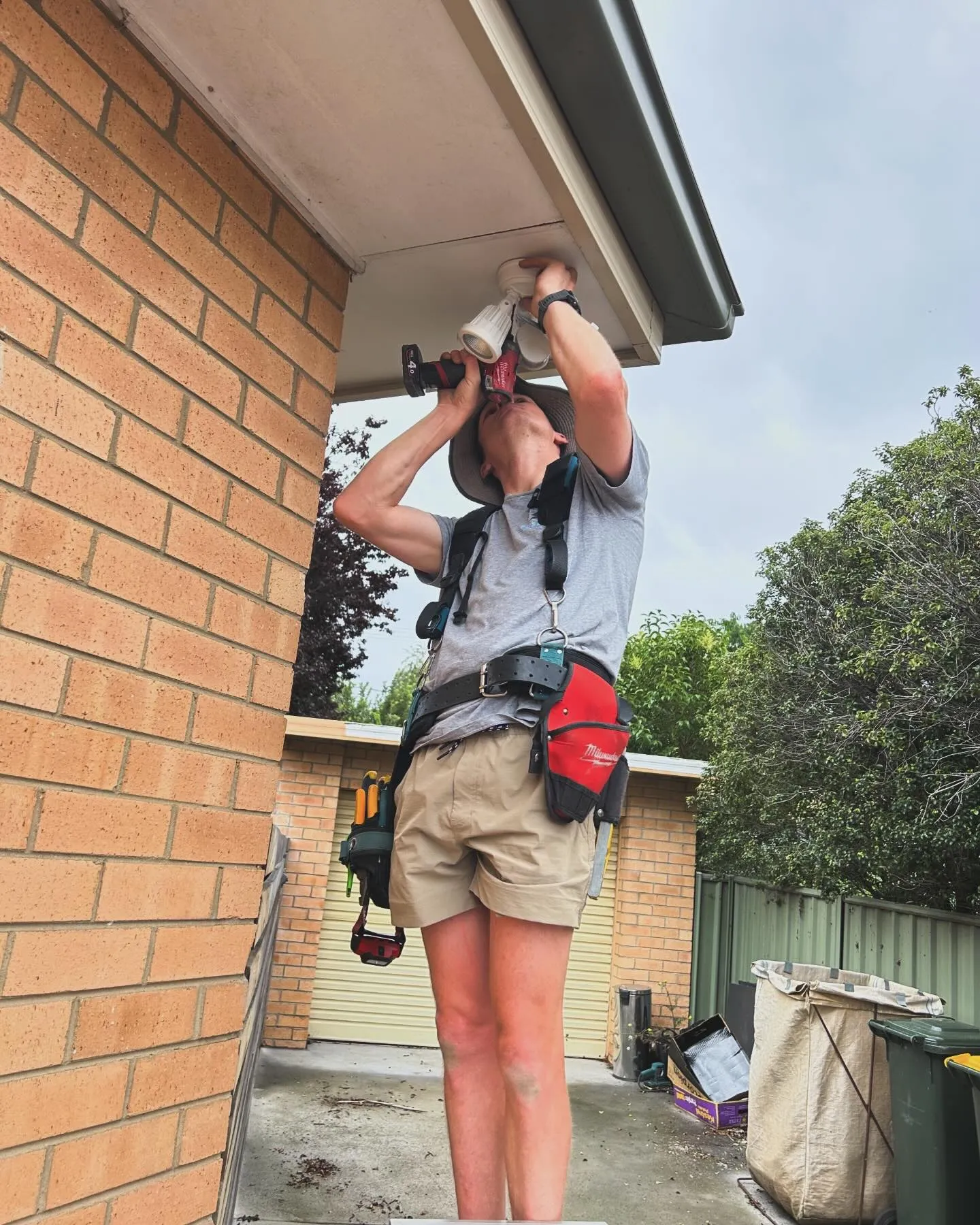 Electrician fitting a ceiling-mounted fitting under the eave of a brick Canberra home