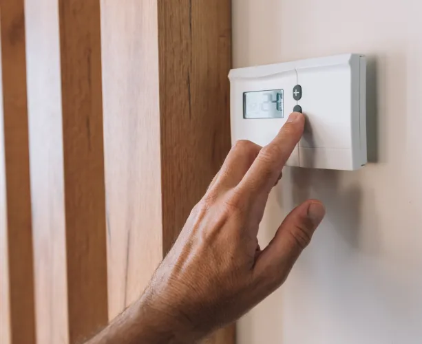 Hand pressing the button on a home heating and cooling controller